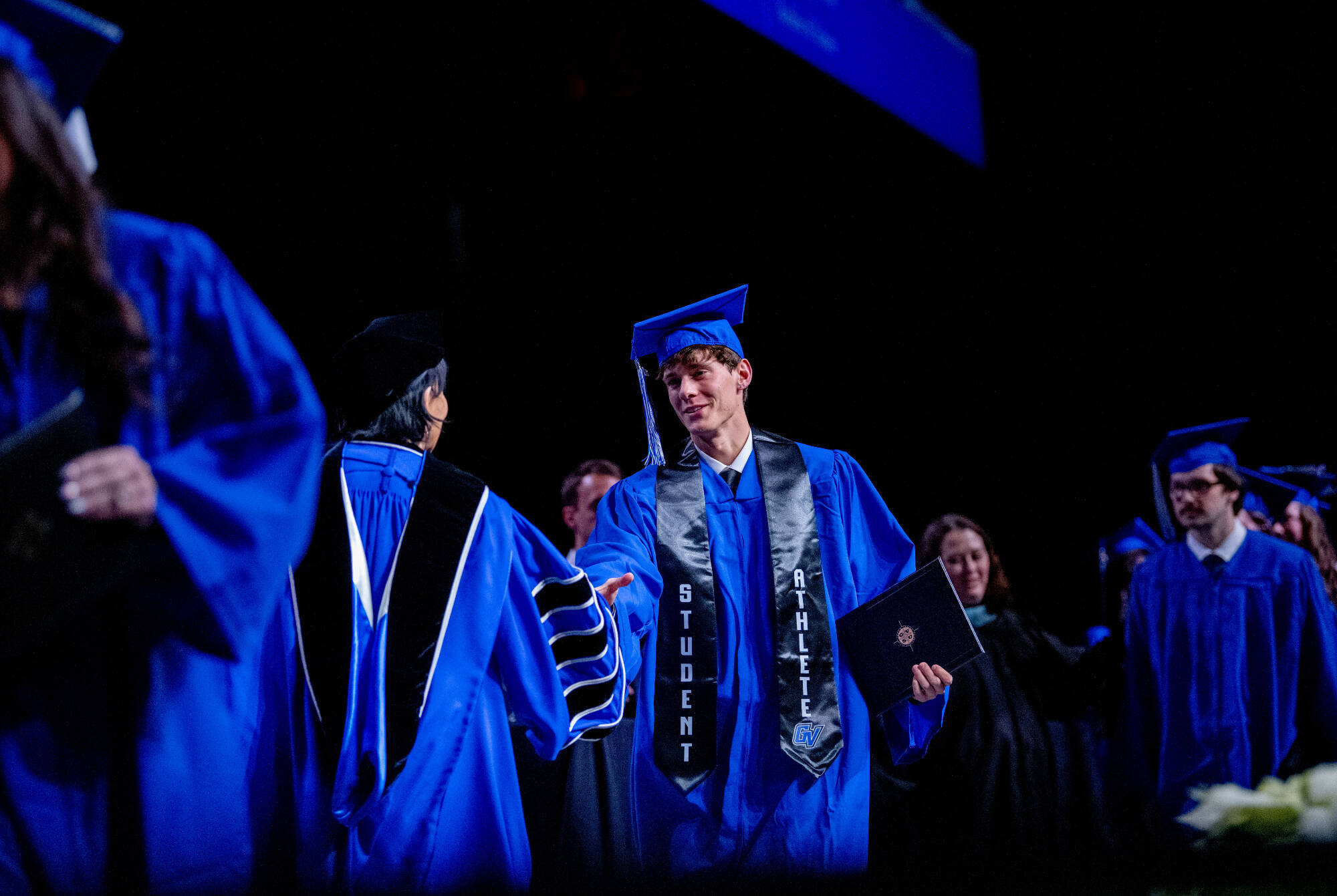A graduate walks across stage at commencement and shakes President Mantellas hand